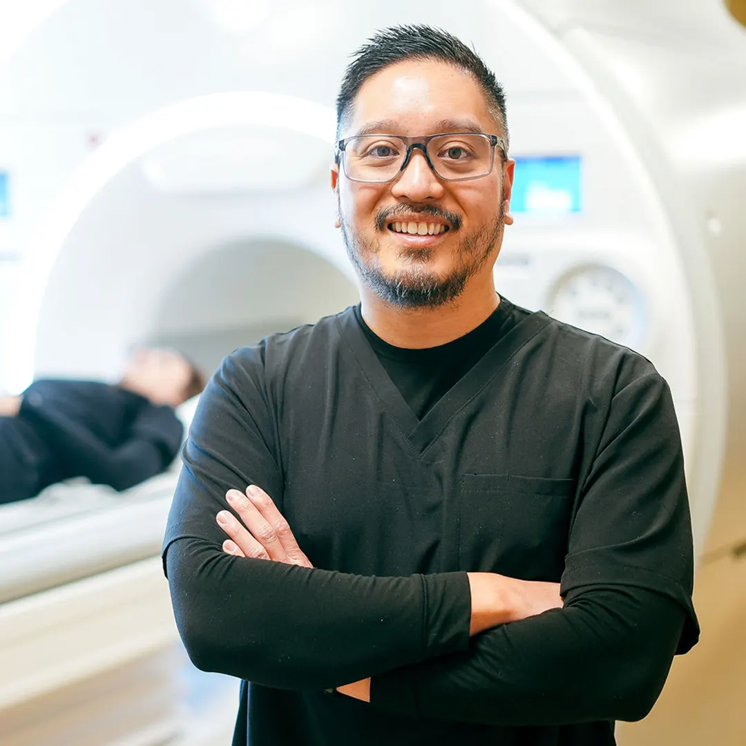 Healthcare professional in scrubs posing in an MRI exam room